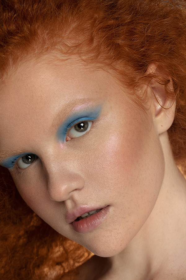 Ginger girl with very light skin and blue eyeshadow in beauty product campaign